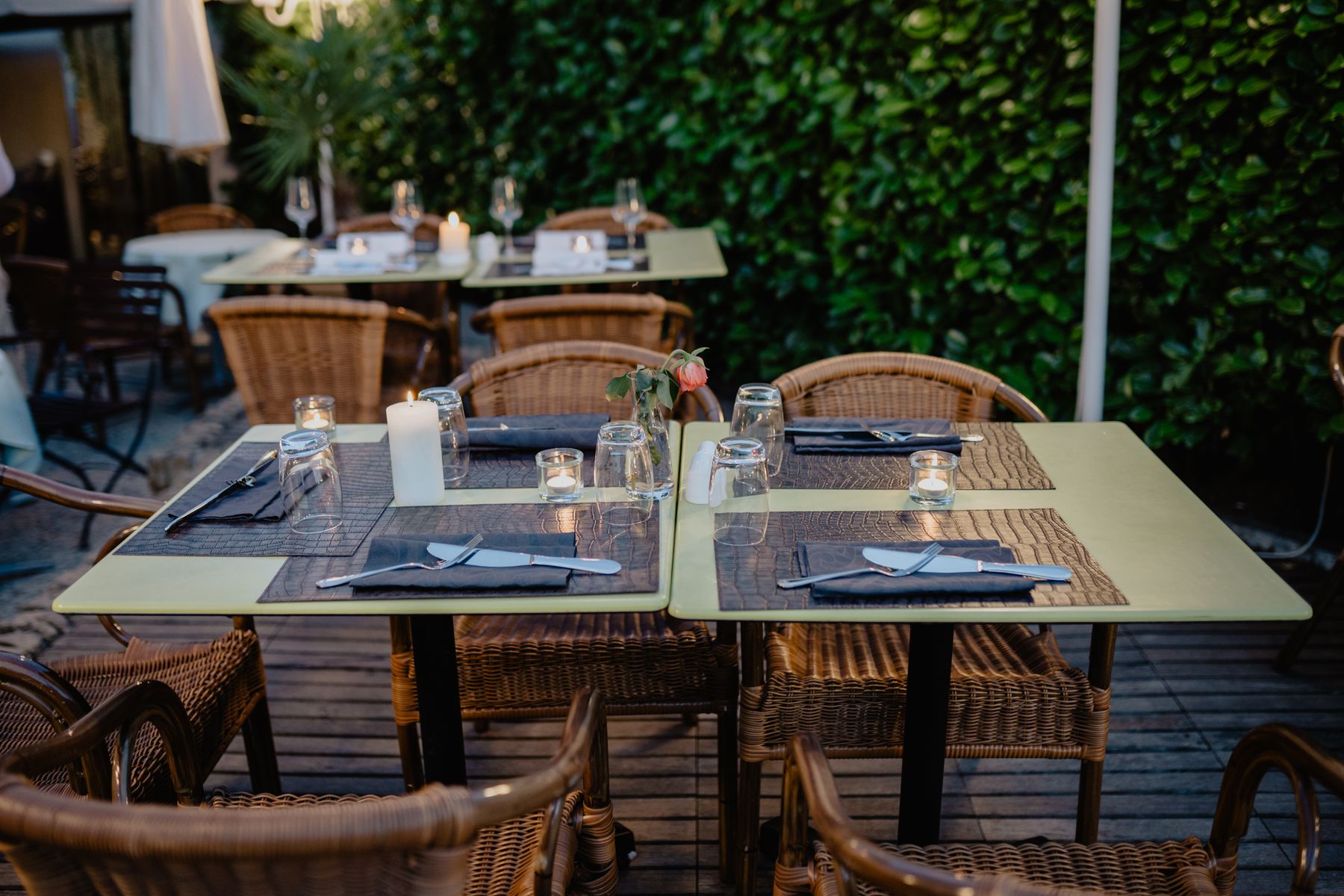 Gedeckte Tische mit Kerzen auf der Terrasse, dahinter eine dichte Hecke